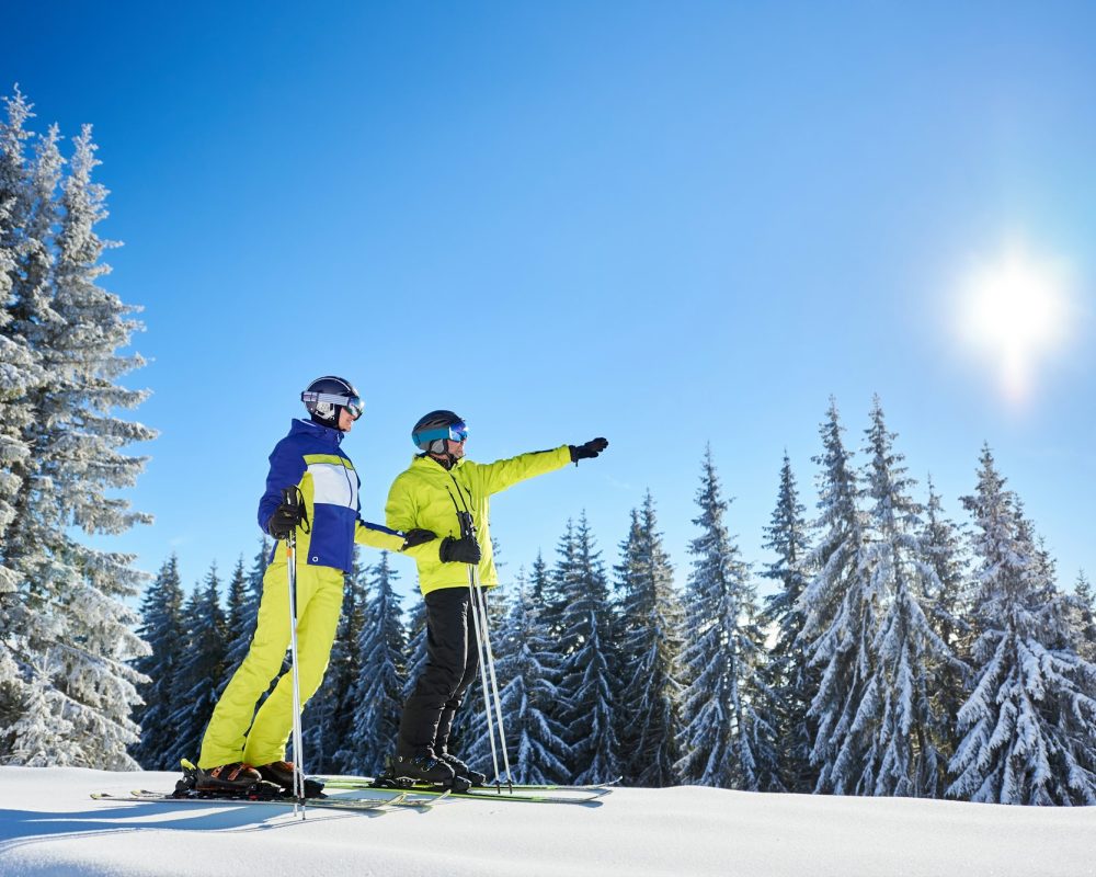 Couple of skiers on skis on hill at ski resort. Recreational activities in mountains concept.